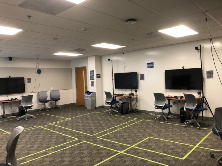 instructional space with monitors on the wall and neon grid sectioning the floor into squares for VR users to stand in