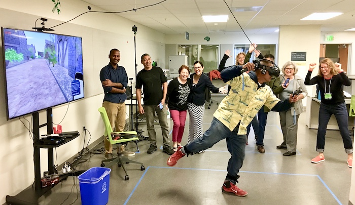 a crowd gathers around a person using a virtual reality headset with their limbs splayed out in an active motion