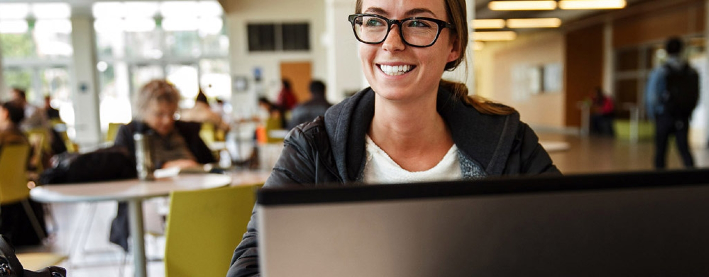 smiling student on laptop in JPLL lobby cafe