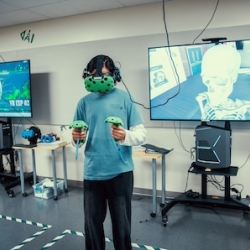 a person wearing a vr headset and holding controllers, while another person watches